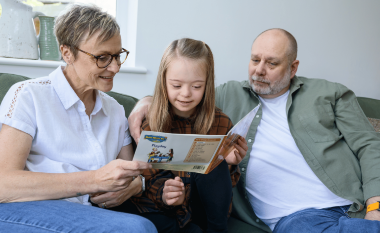 Young adopted child sat reading a book with her adoptive parents