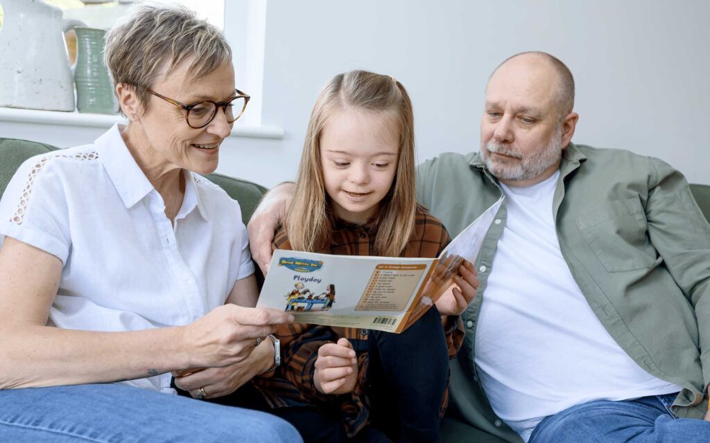 Young adopted child sat reading a book with her adoptive parents